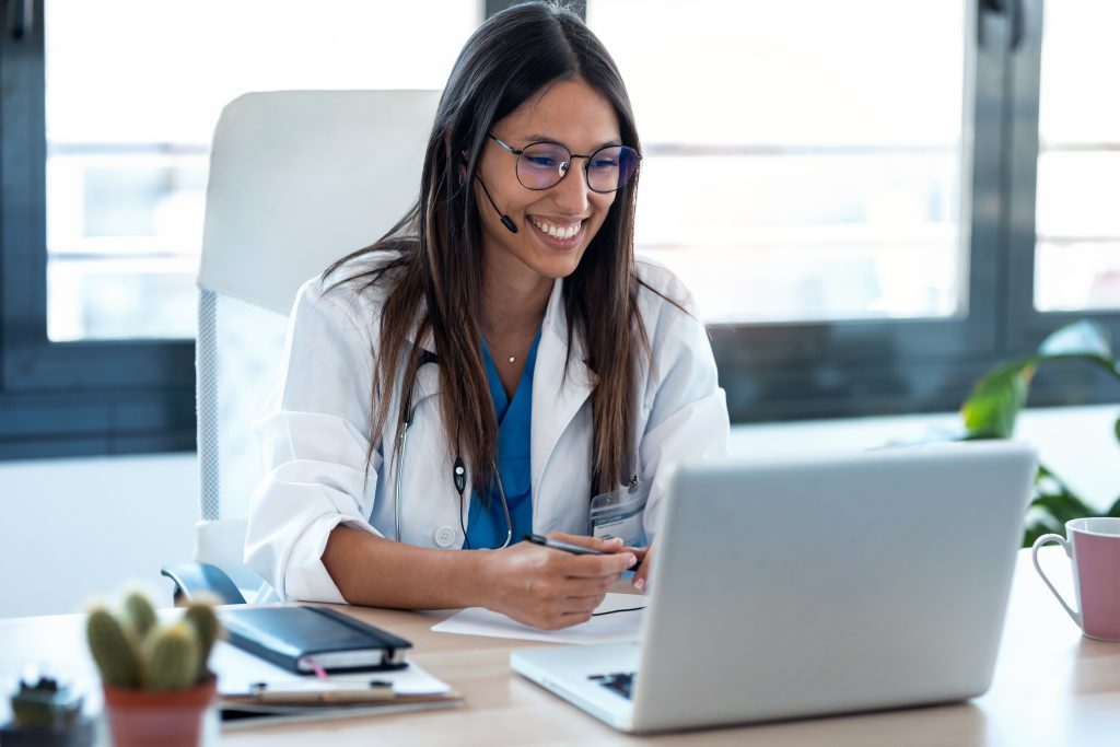 A doctor in a lab coat doing a video call at her desk